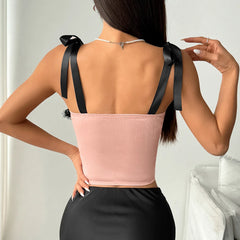 Woman wearing a pink top with black ribbon straps against a neutral background