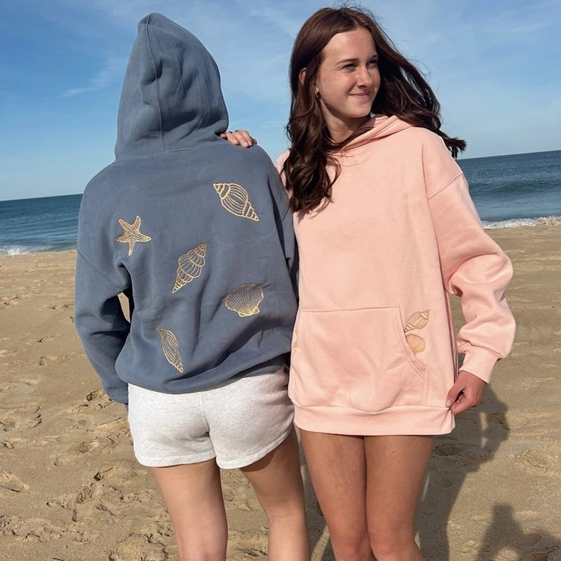 Two people wearing hoodies with shell designs on a beach