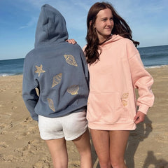Two people wearing hoodies with shell designs on a beach