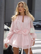 Woman wearing a pink dress with a floral detail on a city street.