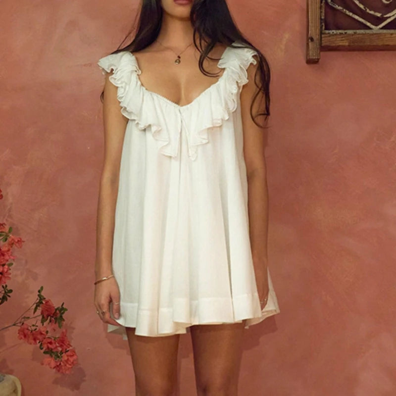 Woman wearing a white dress with ruffled details against a pink wall.