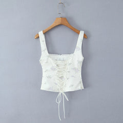 White floral lace-up crop top on a wooden hanger against a gray background