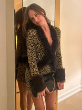 Woman wearing a leopard print outfit with fur trim in front of a mirror.