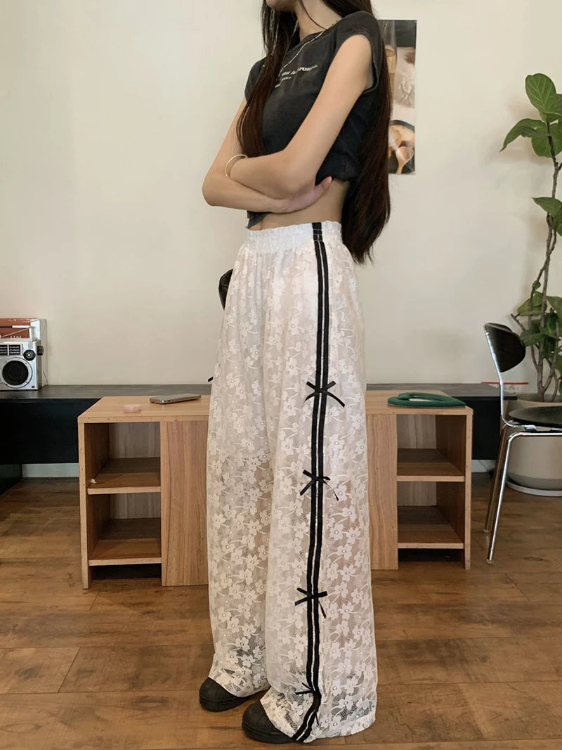 Person wearing a black top and white lace pants with black ribbons in a room.