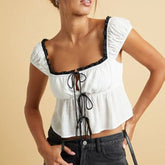 Woman wearing a white top with black lace details on a beige background