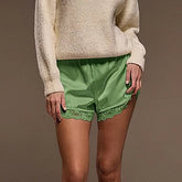 Person wearing green satin shorts and a beige sweater against a brown background