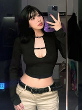 Person taking a mirror selfie wearing a black top with cut-out design and beige pants.