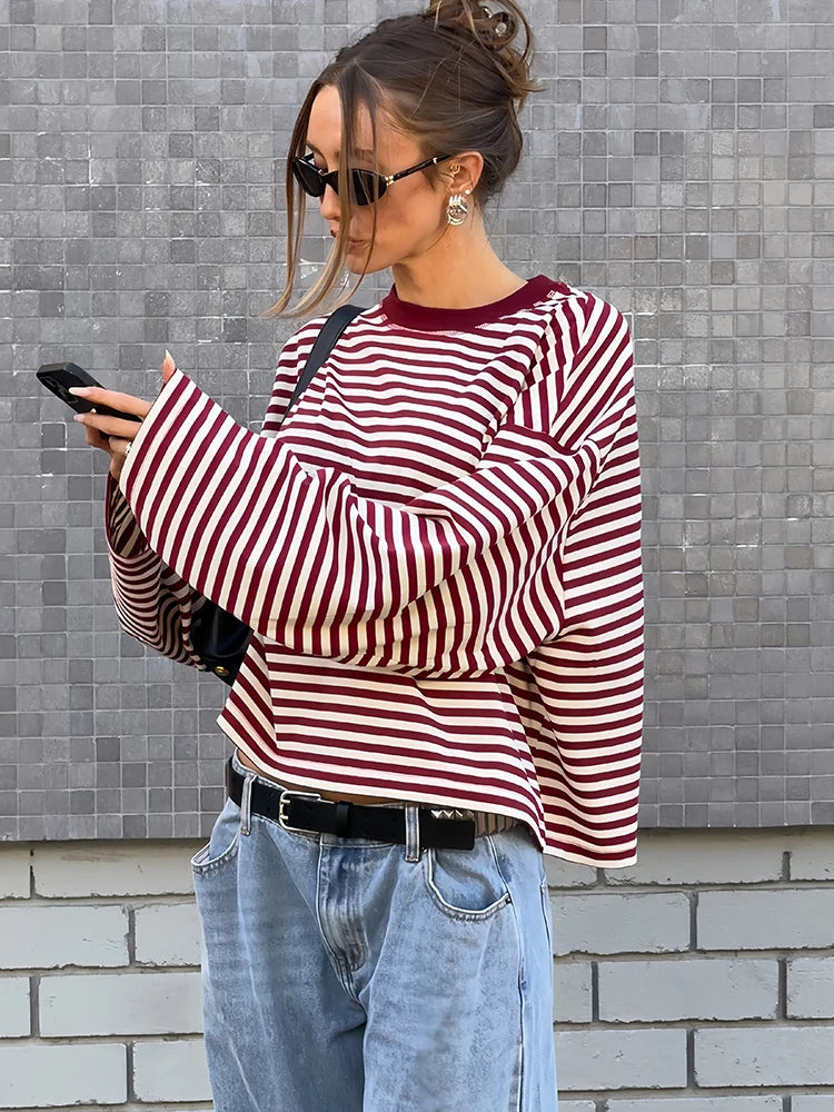 Woman wearing a red and white striped sweater and blue jeans, standing against a tiled wall.