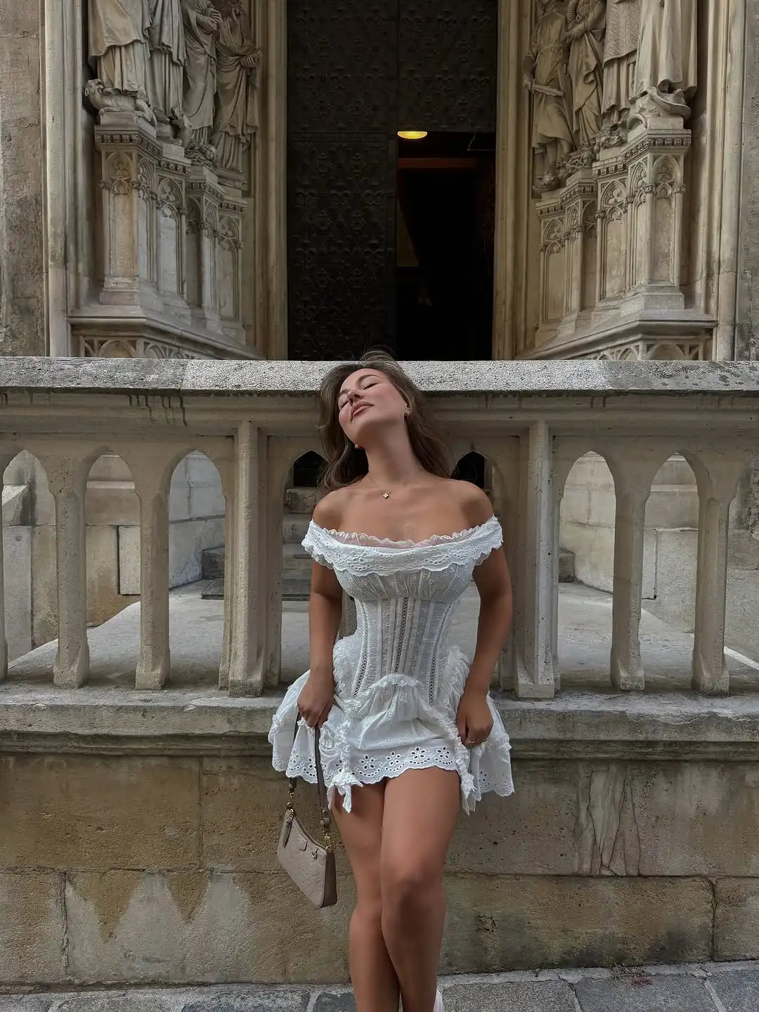 Woman in a white dress standing on a stone balcony with architectural background