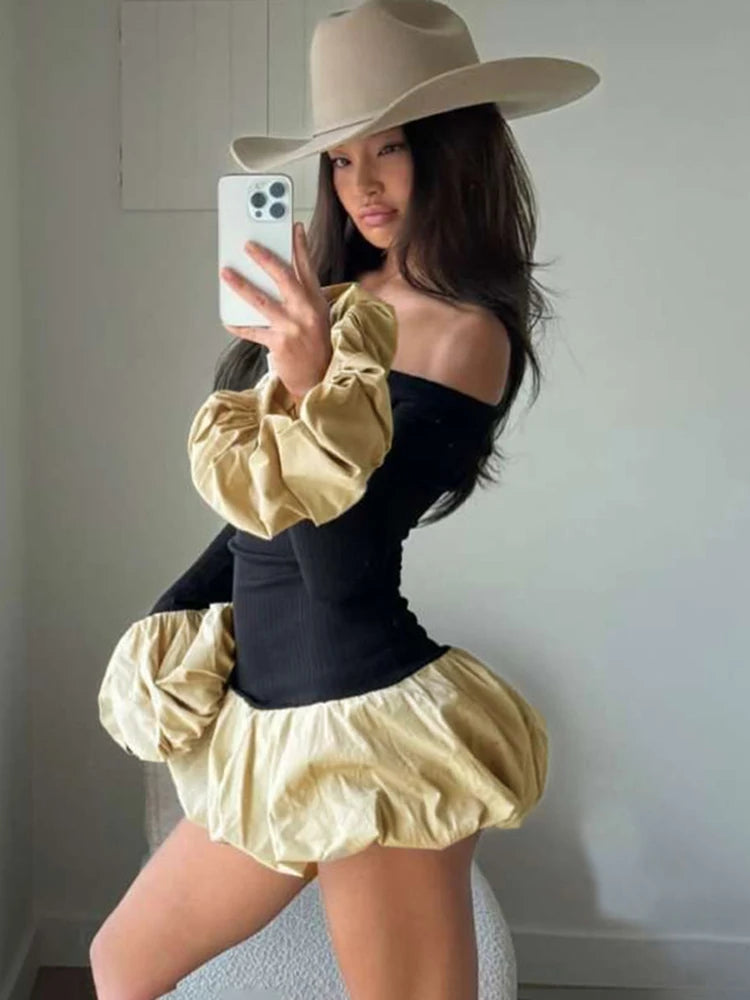Person wearing a black top with gold ruffled sleeves and skirt, beige hat, taking a mirror selfie.