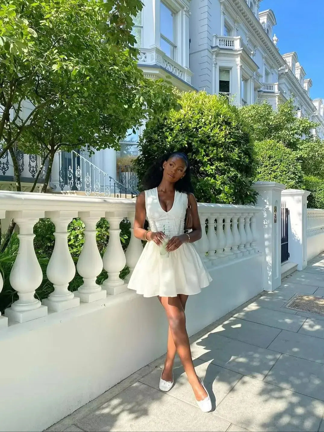 Woman in a white dress standing in front of a classical building with greenery.