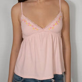 Pink spaghetti strap top with floral embroidery on a plain background