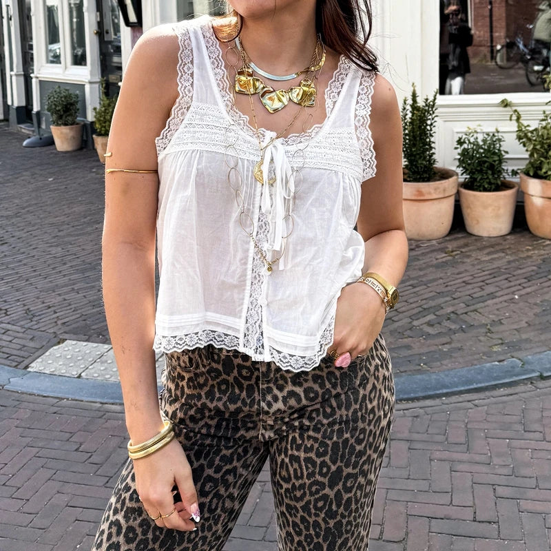 Woman wearing a white lace top and leopard print pants on a street.
