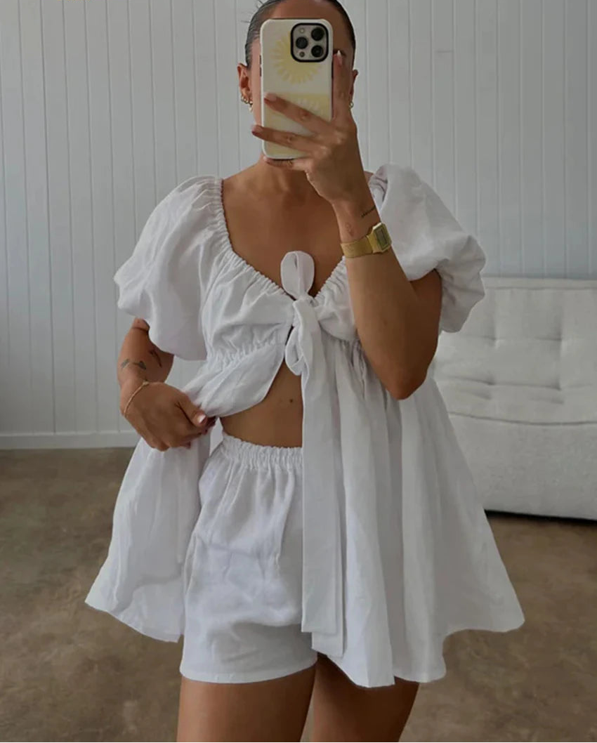 Person wearing a white outfit with puffed sleeves and tied neckline, standing in a room.