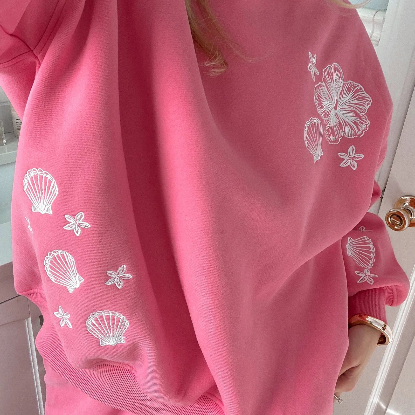 Pink sweatshirt with white shell and flower patterns worn by a person.