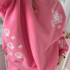 Pink sweatshirt with white shell and flower patterns worn by a person.