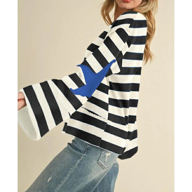 Black and white striped sweater with a blue accent held by a person against a beige background