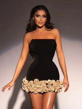 Woman wearing a black strapless dress with floral details on a plain background