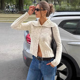 Woman wearing a beige cardigan and blue jeans standing next to a car outdoors.