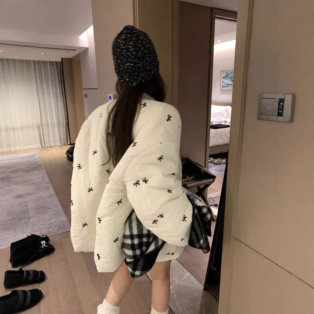 Person wearing a white quilted jacket with black bee patterns in a room.