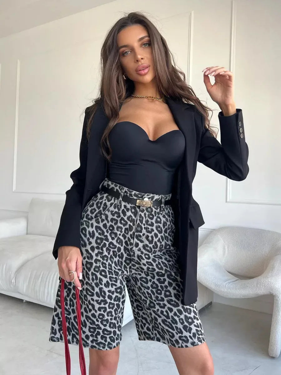 Woman wearing a black blazer, black top, and leopard print shorts in a minimalistic room.