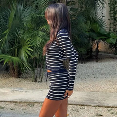 Person wearing a black and white striped dress standing in a garden with green plants.