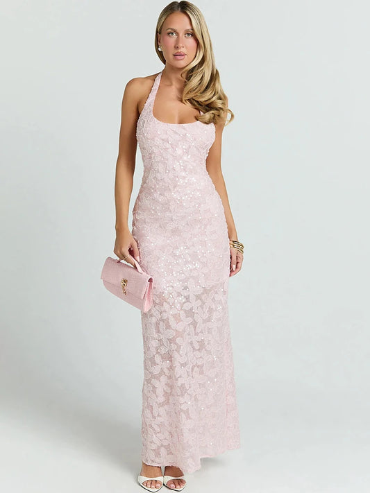 Woman wearing a light pink sequin halter maxi dress with 3D floral details and holding a pink clutch.