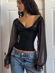 Woman wearing a black top with sheer sleeves and blue jeans indoors.