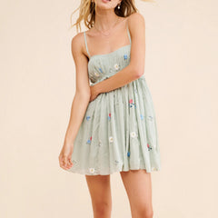 Woman wearing a light green dress with floral embroidery on a beige background