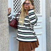 Woman wearing a striped shirt and brown skirt standing in front of a white door.