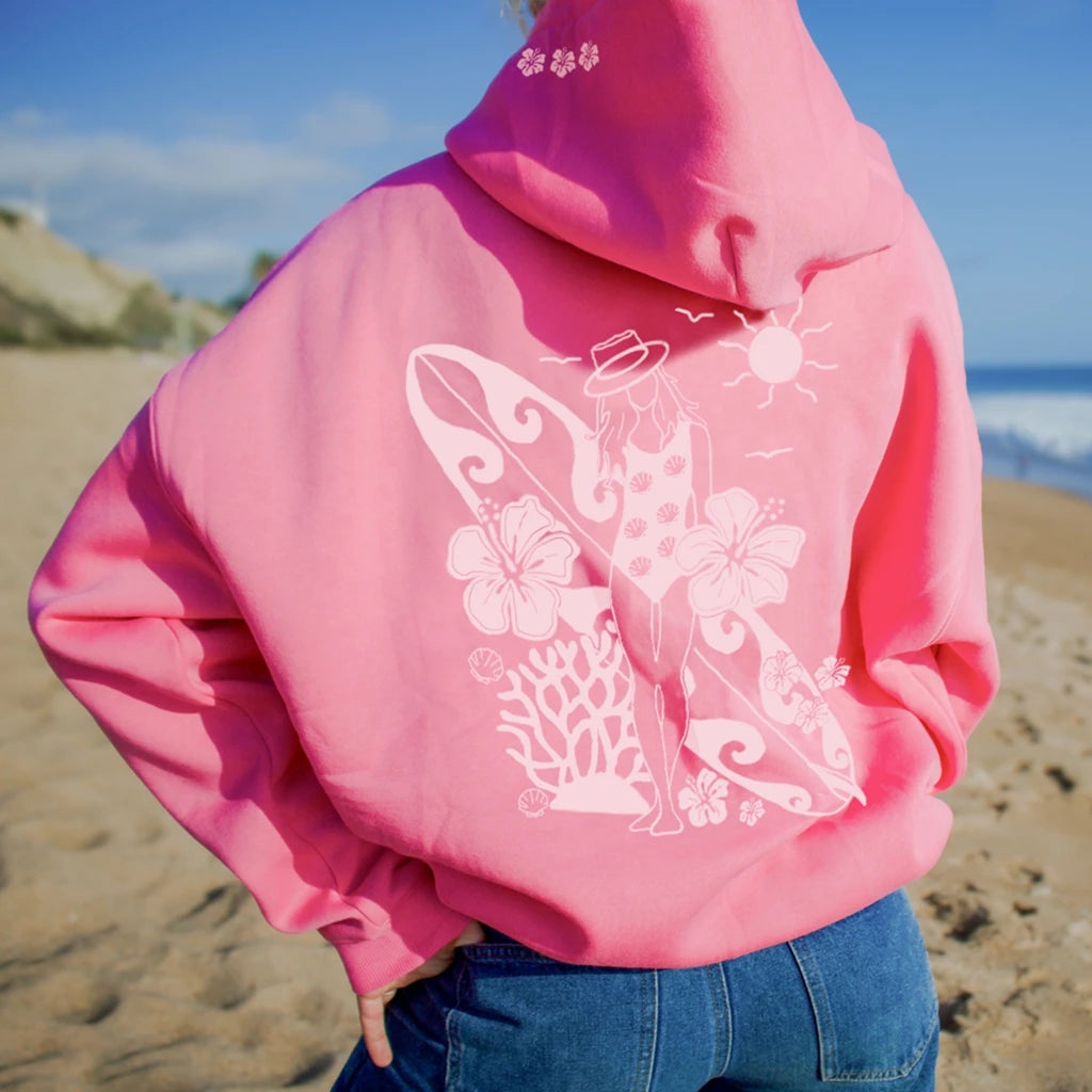 Person wearing a pink hoodie with a beach-themed design on a sandy background