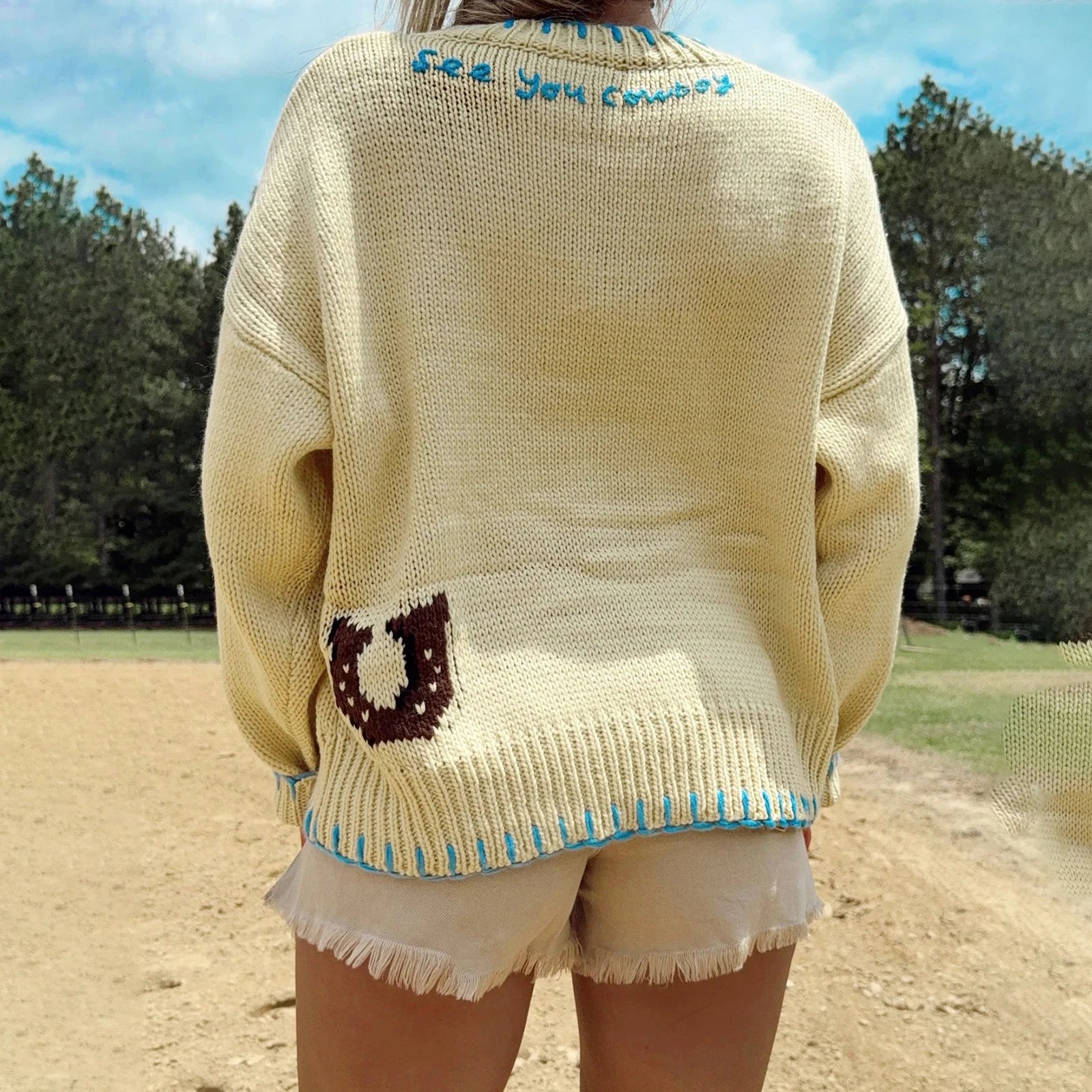 Person wearing a beige sweater with text and graphics outdoors