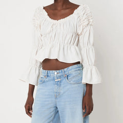 Person wearing a white blouse with ruffled details and light blue jeans on a plain background