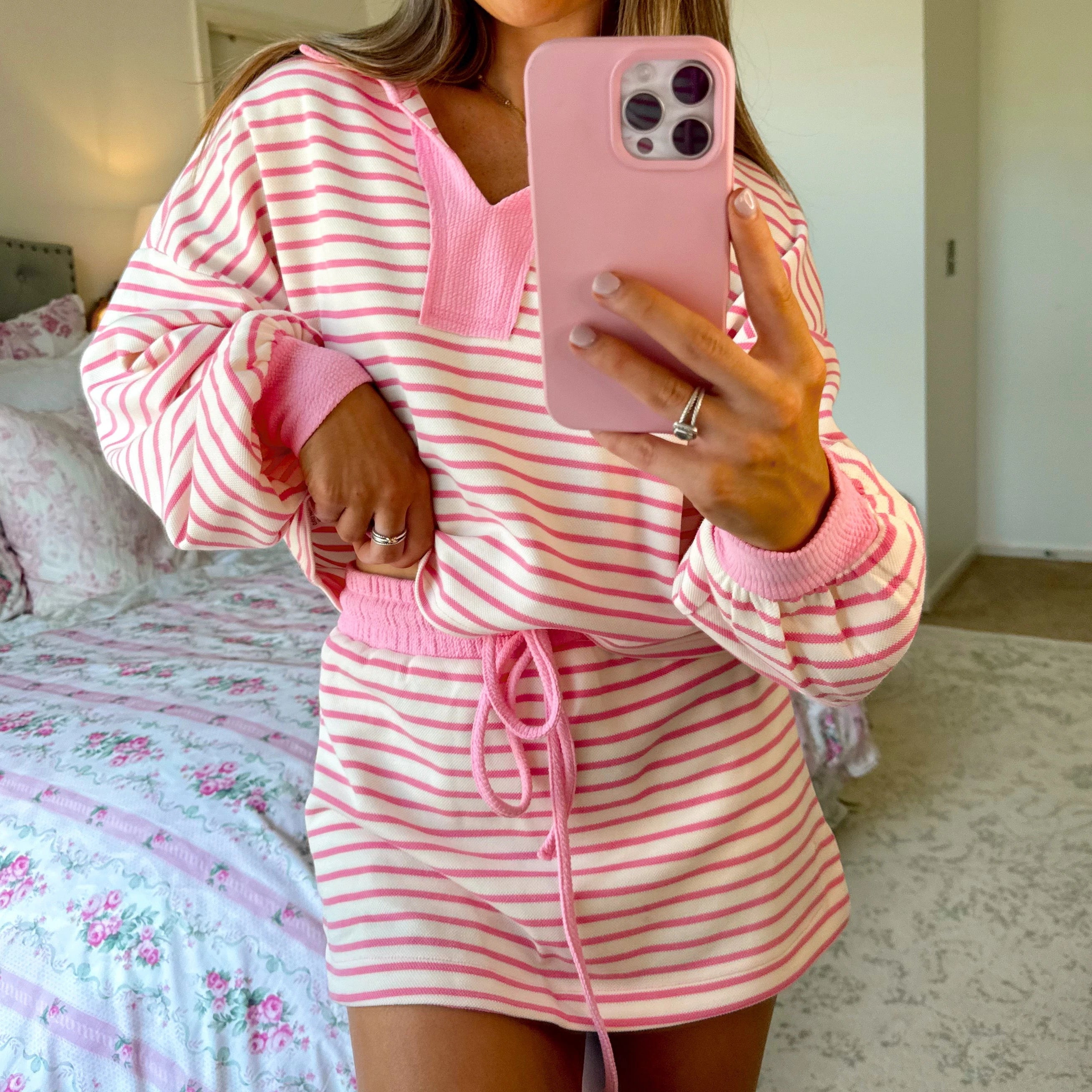 Person wearing a pink and white striped pajama set taking a mirror selfie.