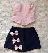 Pink corset top and black skirt with pink bows on a textured surface