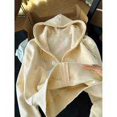 Beige hoodie held by a hand with a cardboard box in the background