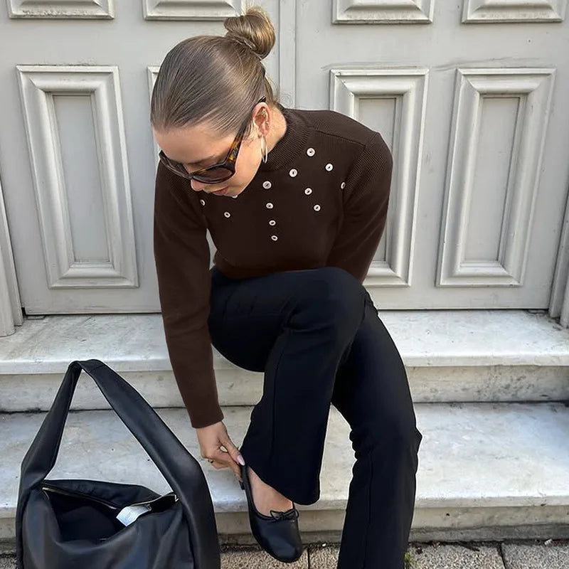 Person in a brown sweater with button details and black pants sitting on steps.