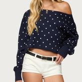 Navy blue off-shoulder top with white polka dots worn by a person on a light gray background