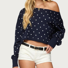 Navy blue off-shoulder top with white polka dots worn by a person on a light gray background