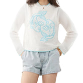 Person wearing a white sweater with blue embroidery and denim shorts
