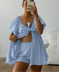 Woman taking a mirror selfie wearing a light blue outfit with a white wall background