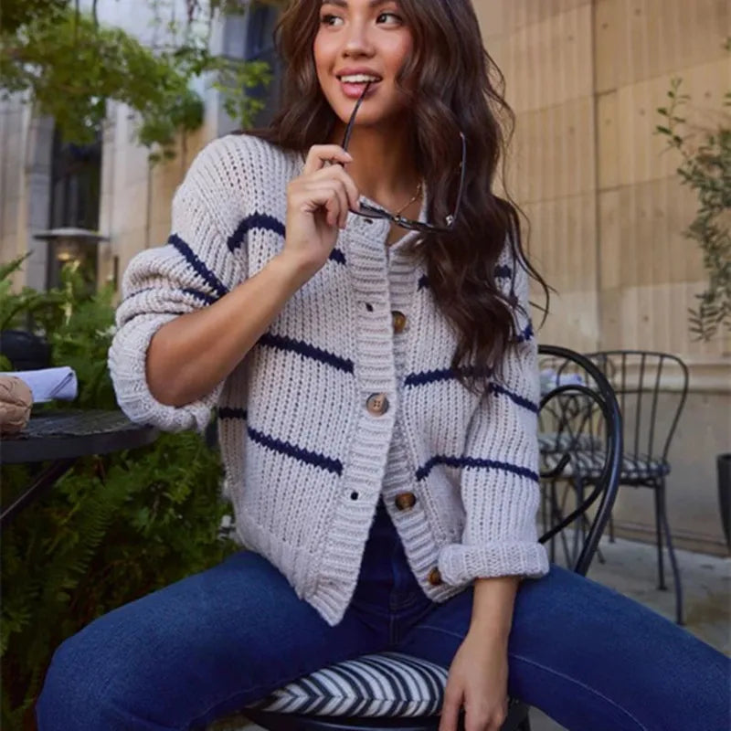 Woman wearing a white cardigan with blue stripes sitting outdoors.