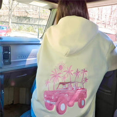 Person wearing a light green hoodie with a pink truck and palm tree design inside a vehicle.