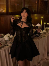 Woman in a black dress standing in a dimly lit room with tables and candles.
