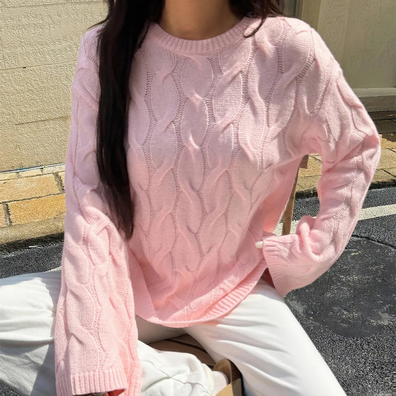Person wearing a pink cable knit sweater sitting outdoors.