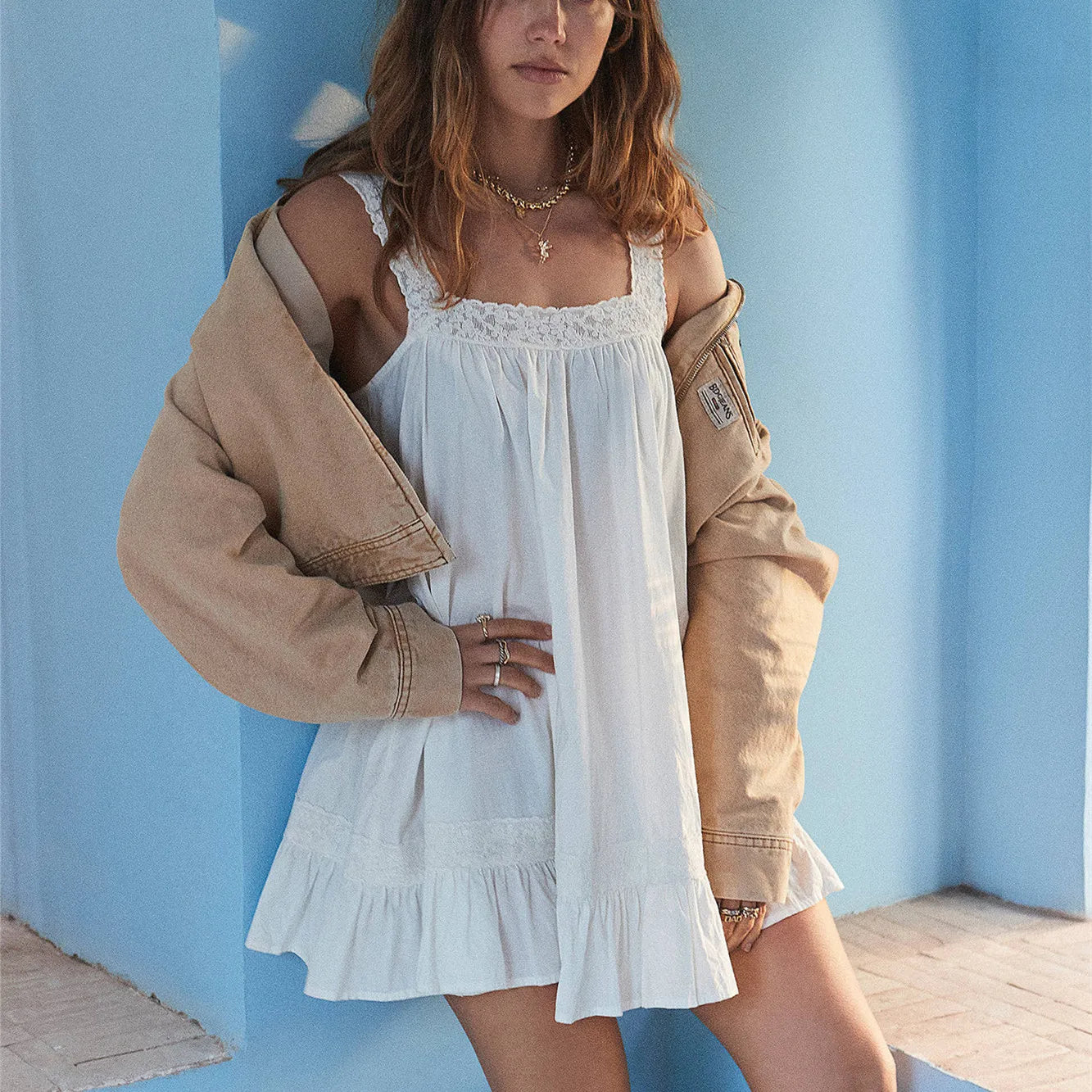 Woman wearing a white dress with a beige jacket against a blue wall