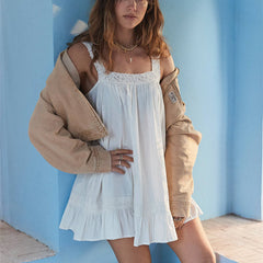 Woman wearing a white dress with a beige jacket against a blue wall