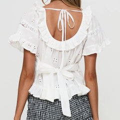 White blouse with ruffled back and tied front on a plain background