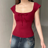 Red top with a bow detail worn by a person against a neutral background