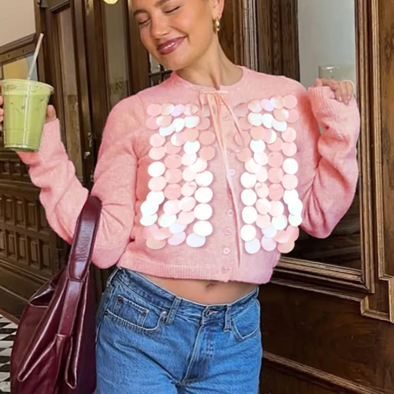 Woman wearing a pink sweater with white circular patterns, holding a green smoothie.